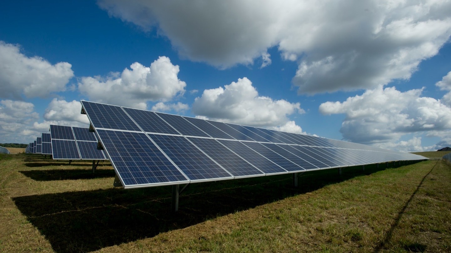 A long row of ground-mounted solar panels standing over a green grass field